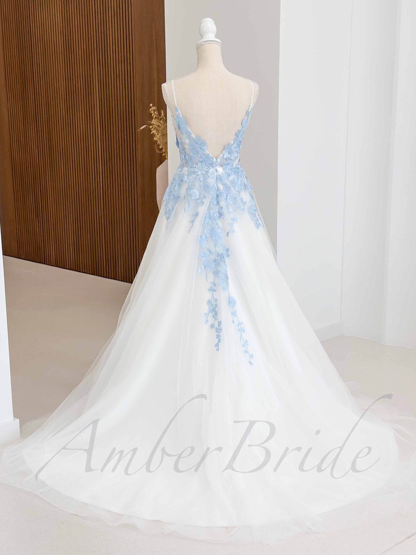 Back view of a white tulle A-line wedding dress with spaghetti straps, open back, and blue floral lace applique.