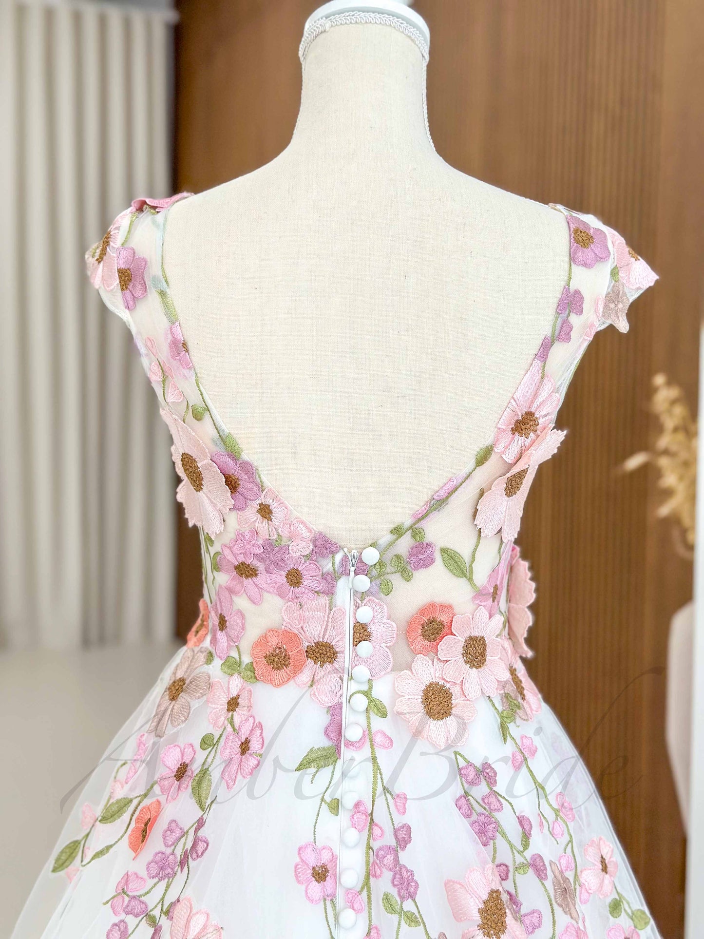 Backless tulle wedding dress with pink floral embroidery, cap sleeves, and a row of buttons down the back.