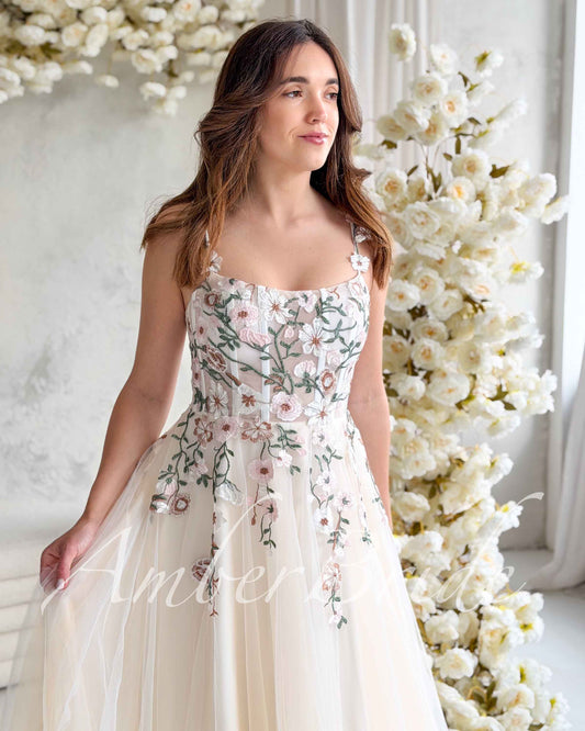 Nude-colored wedding dress with a square neckline, corset bodice, and pastel floral embroidery on tulle fabric.