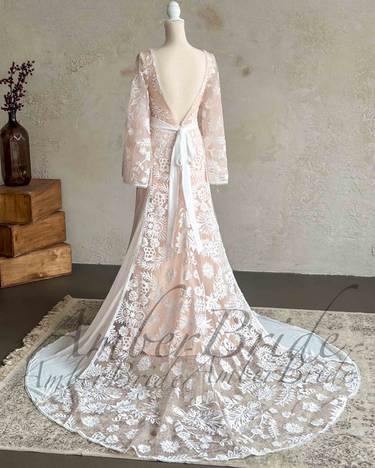 Back view of a boho wedding dress with white floral embroidery, long cape sleeves, an open back, and a tied waist.