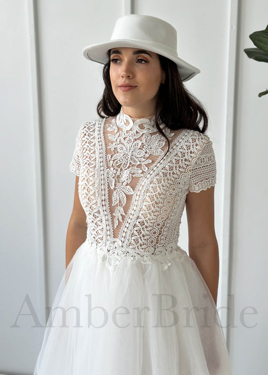 A bride wears a boho A-line dress with a white lace high-neck bodice, short sleeves, and a soft tulle skirt.