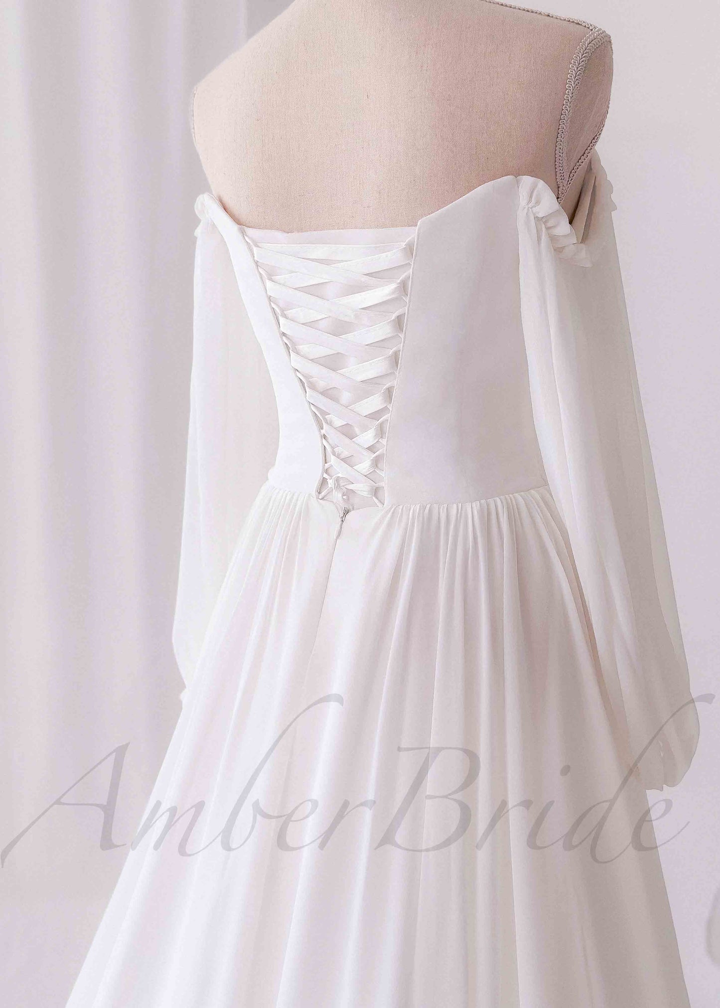 White A-line wedding dress, back view, off-shoulder long sleeves, corset-style lace-up back, and flowing skirt.