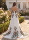 White chiffon wedding dress with off-shoulder sleeves, floral embroidery, and a buttoned back in a garden setting.