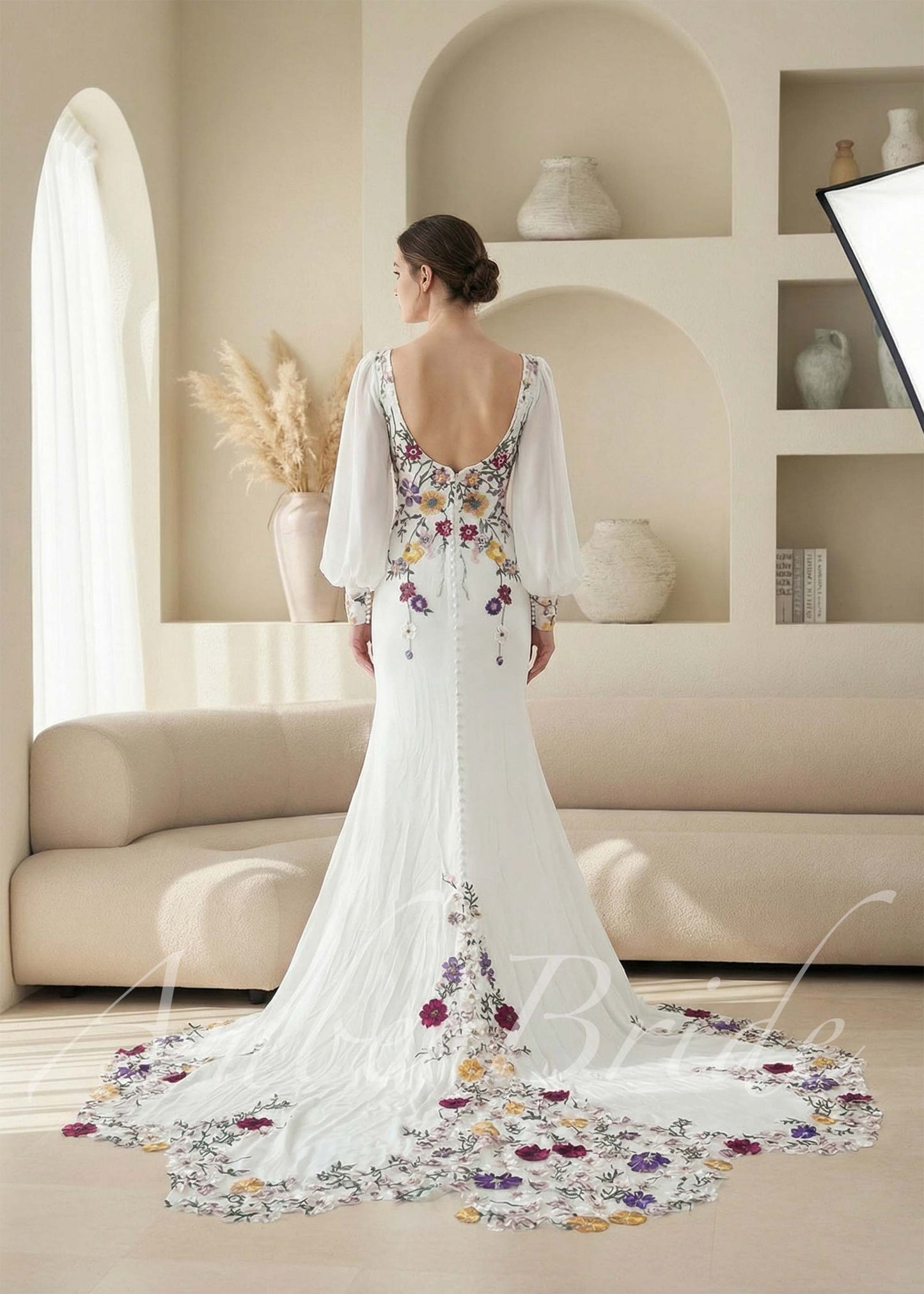 White mermaid bridal gown with backless scoop neck, long puff sleeves, and colorful floral embroidery on train.
