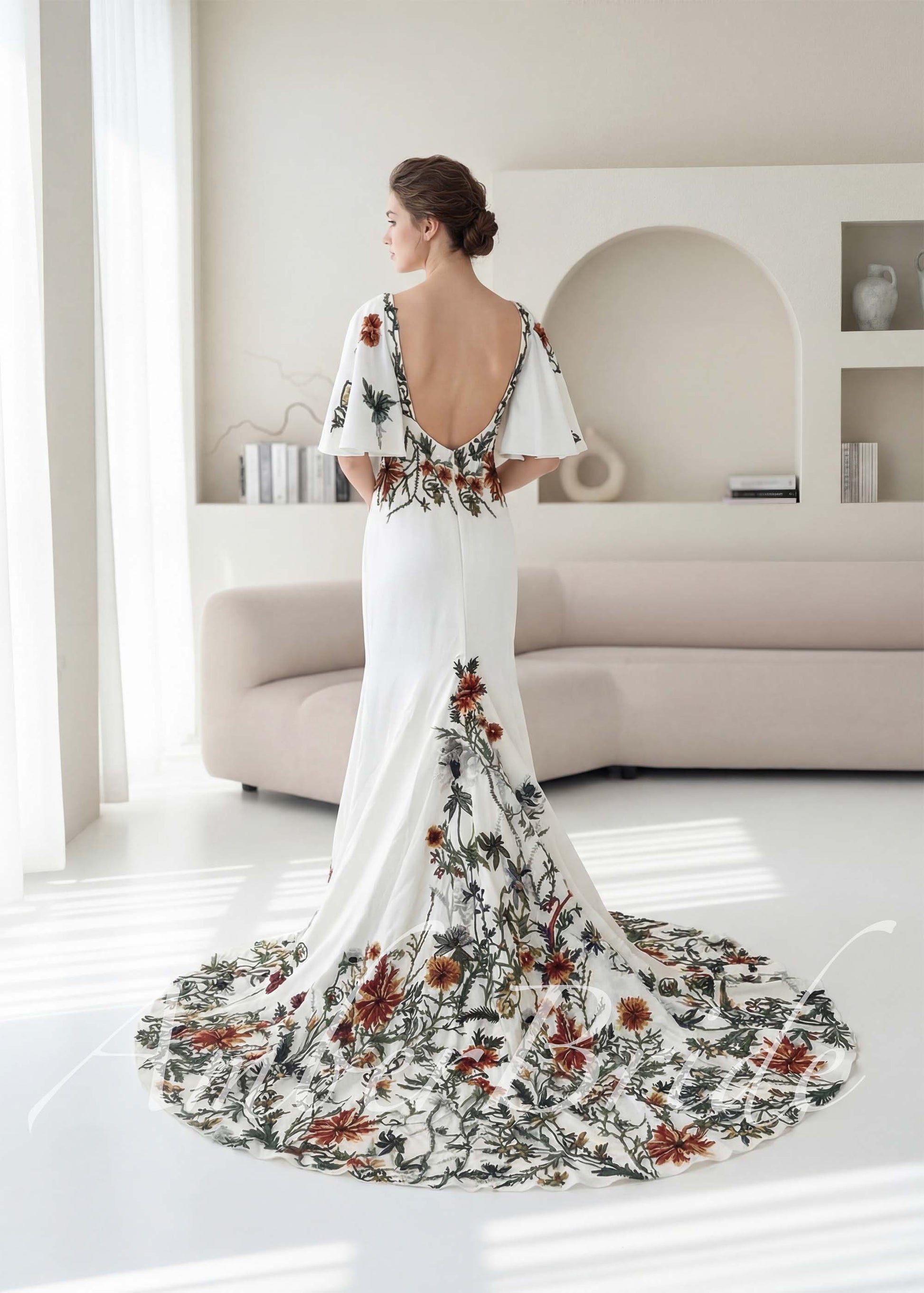 White crepe mermaid wedding dress with open back, flutter sleeves, and colorful earthy floral embroidery on skirt.