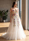 Off-shoulder A-line wedding dress featuring colorful 3D floral appliques and embroidery on a white tulle skirt.