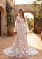 Boho wedding dress with V-neck, cape sleeves, and white floral embroidery over a tan slip in an outdoor courtyard.