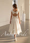 White satin tea-length A-line dress with cap sleeves and a deep open back featuring a single button closure.