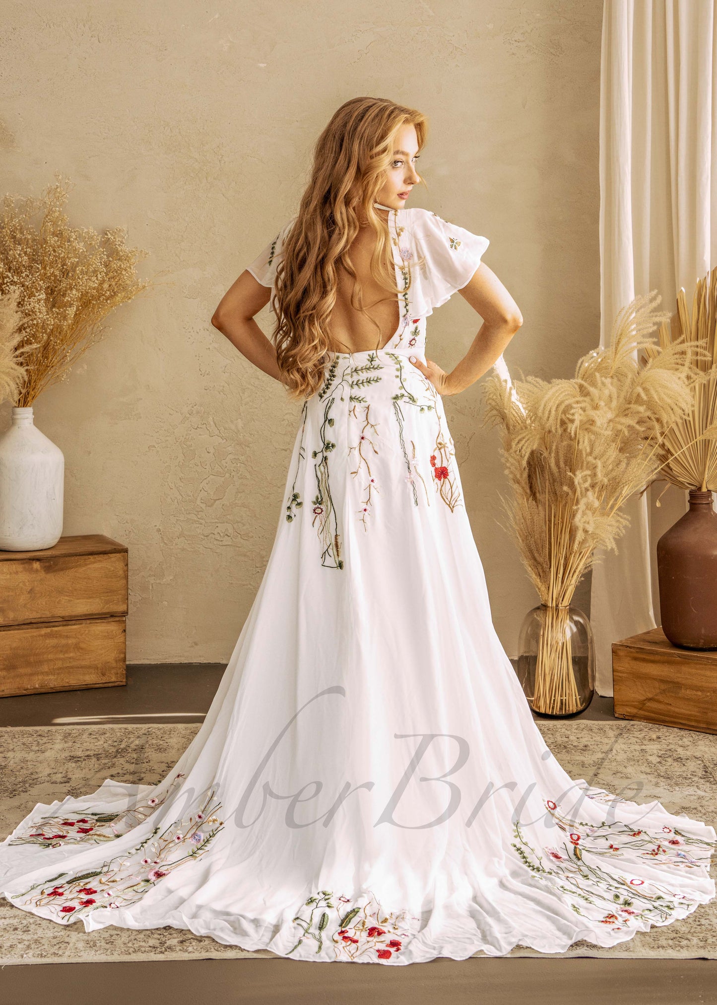 White A-line wedding dress with flutter sleeves, open back, and colorful floral embroidery on the skirt and train.