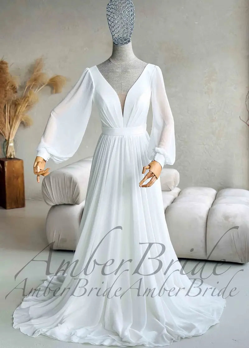 Minimalist white chiffon A-line wedding dress with a deep V-neckline, long sheer bishop sleeves, and a cinched waist.