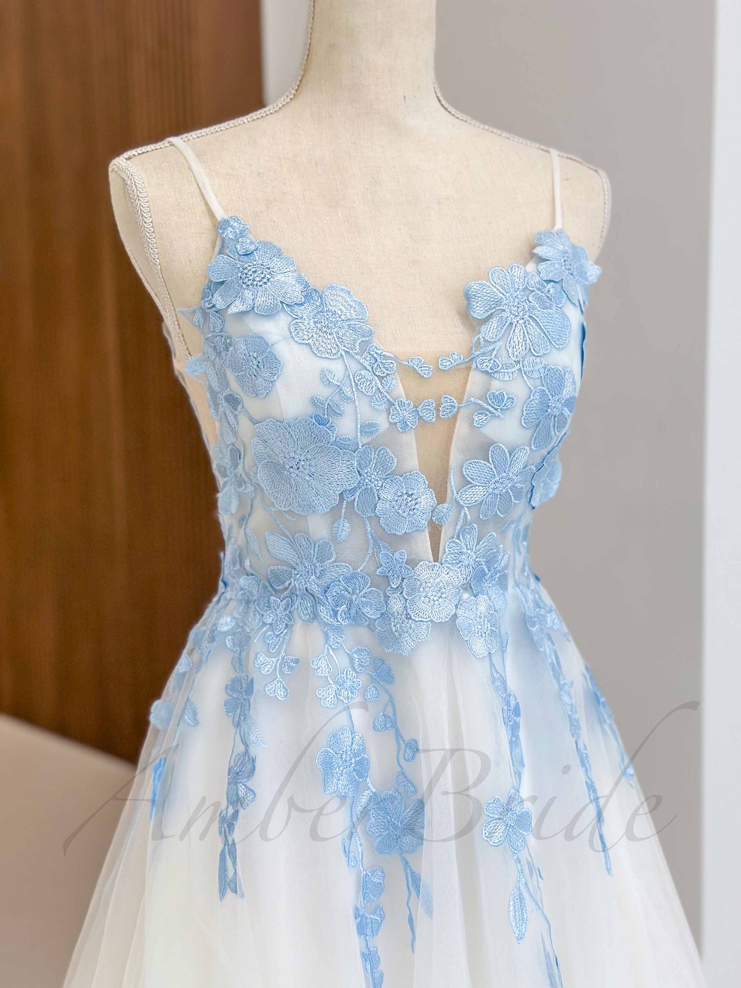Sky blue floral applique on white tulle wedding dress, spaghetti straps, and plunging neckline on a dress form.