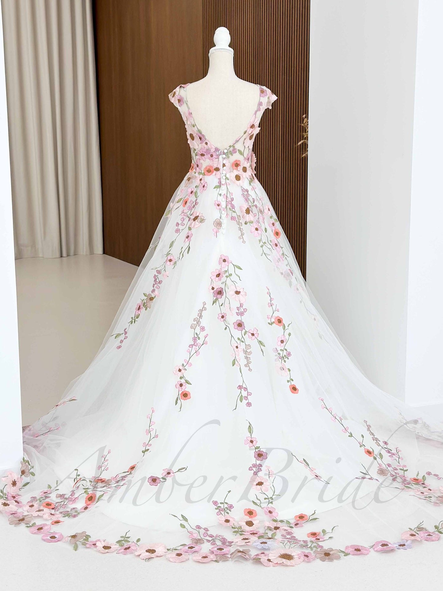 Backless A-line wedding dress in white tulle with pink floral embroidery and a button-up back on a mannequin.
