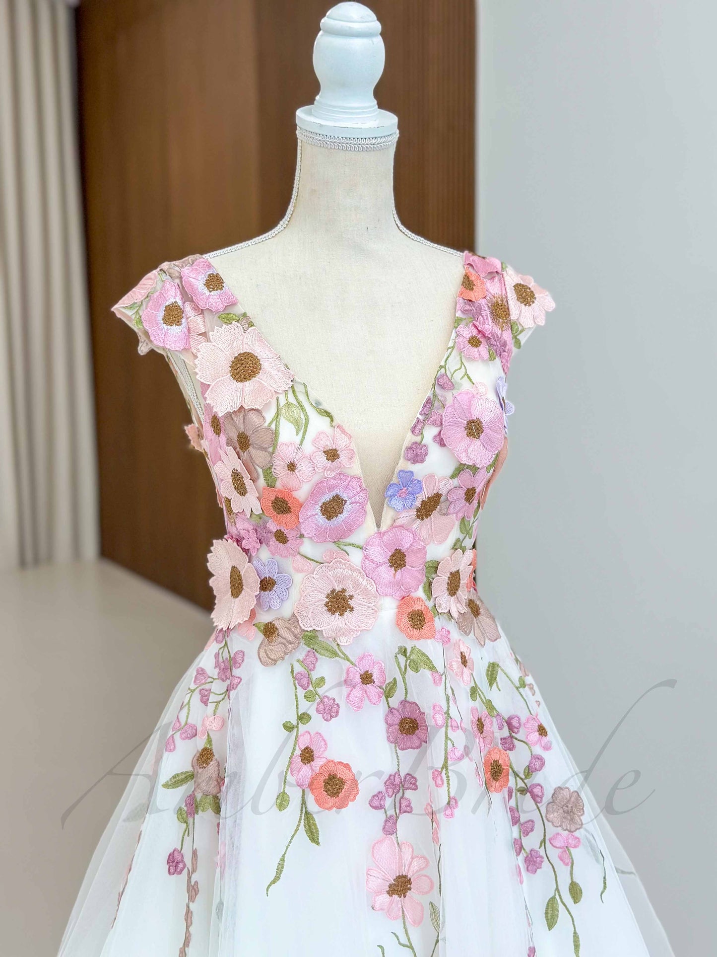 A-line tulle wedding dress with a deep V-neck, cap sleeves, and colorful floral embroidery on a white background.