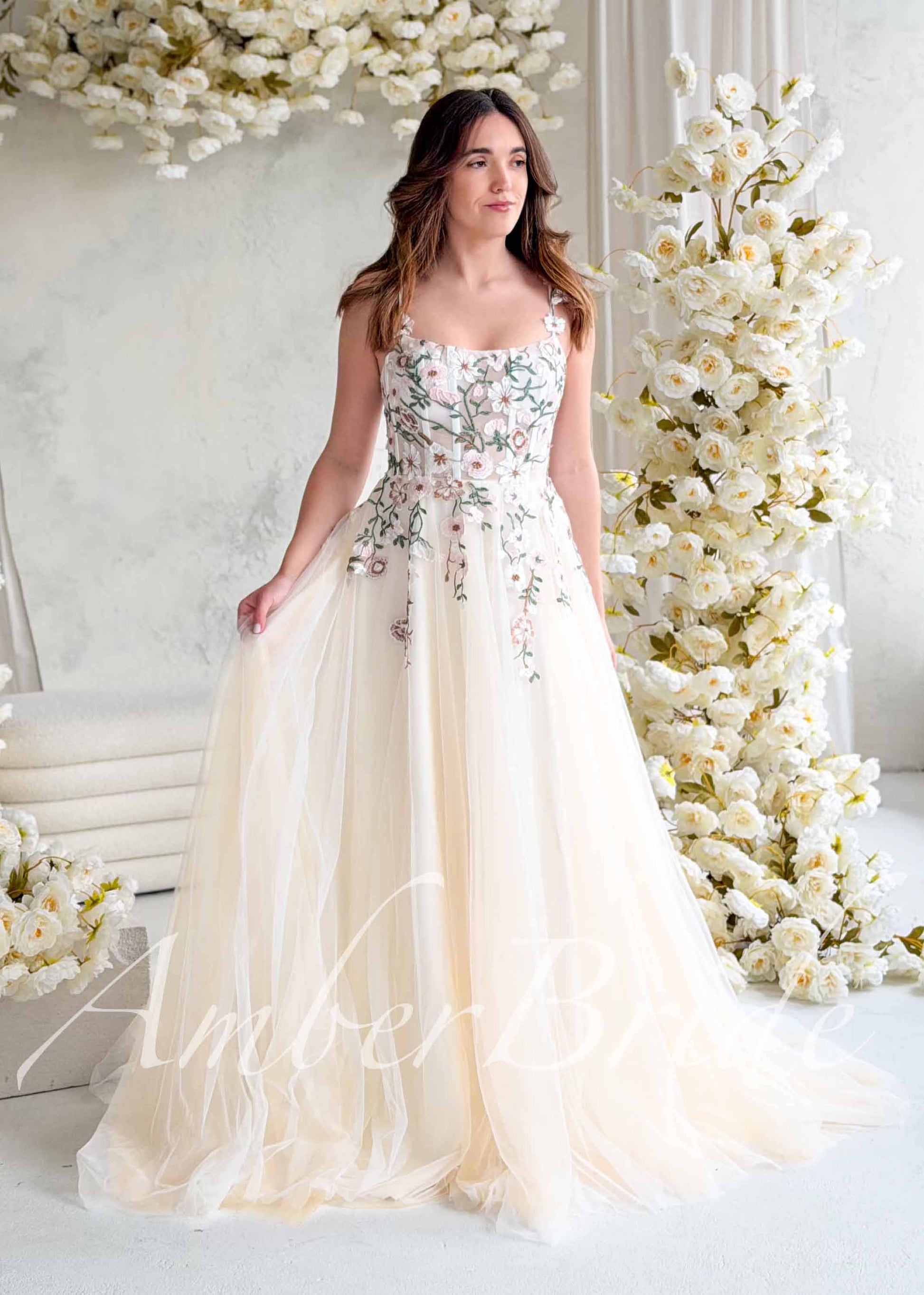 Nude A-line wedding dress with a square neckline, corset bodice, and pastel floral embroidery on layered tulle.