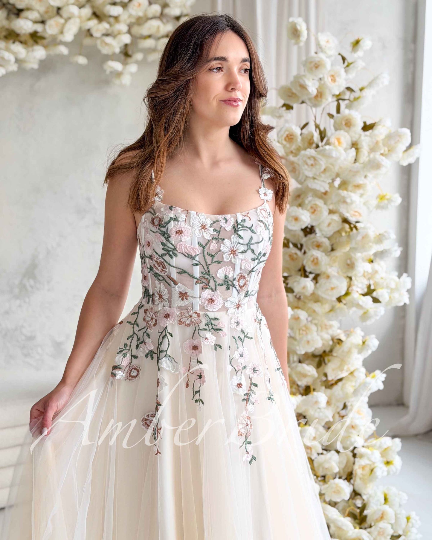 Nude-colored wedding dress with a square neckline, corset bodice, and pastel floral embroidery on tulle fabric.