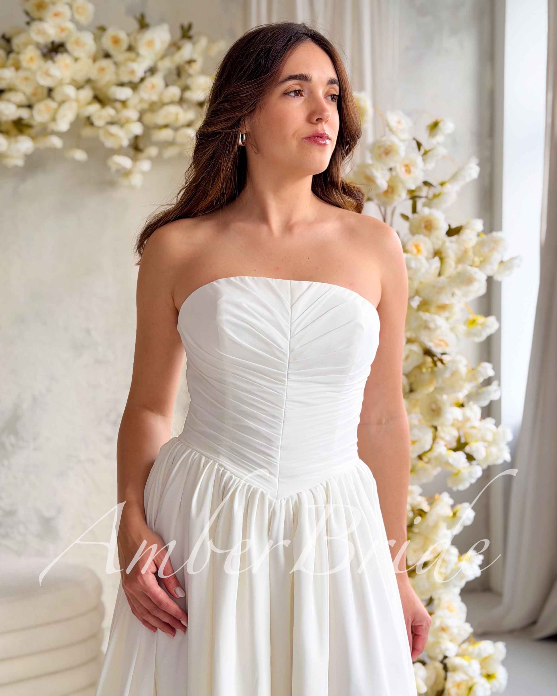 Strapless white chiffon wedding dress featuring a fitted, vertically ruched bodice and a full, flowing skirt.