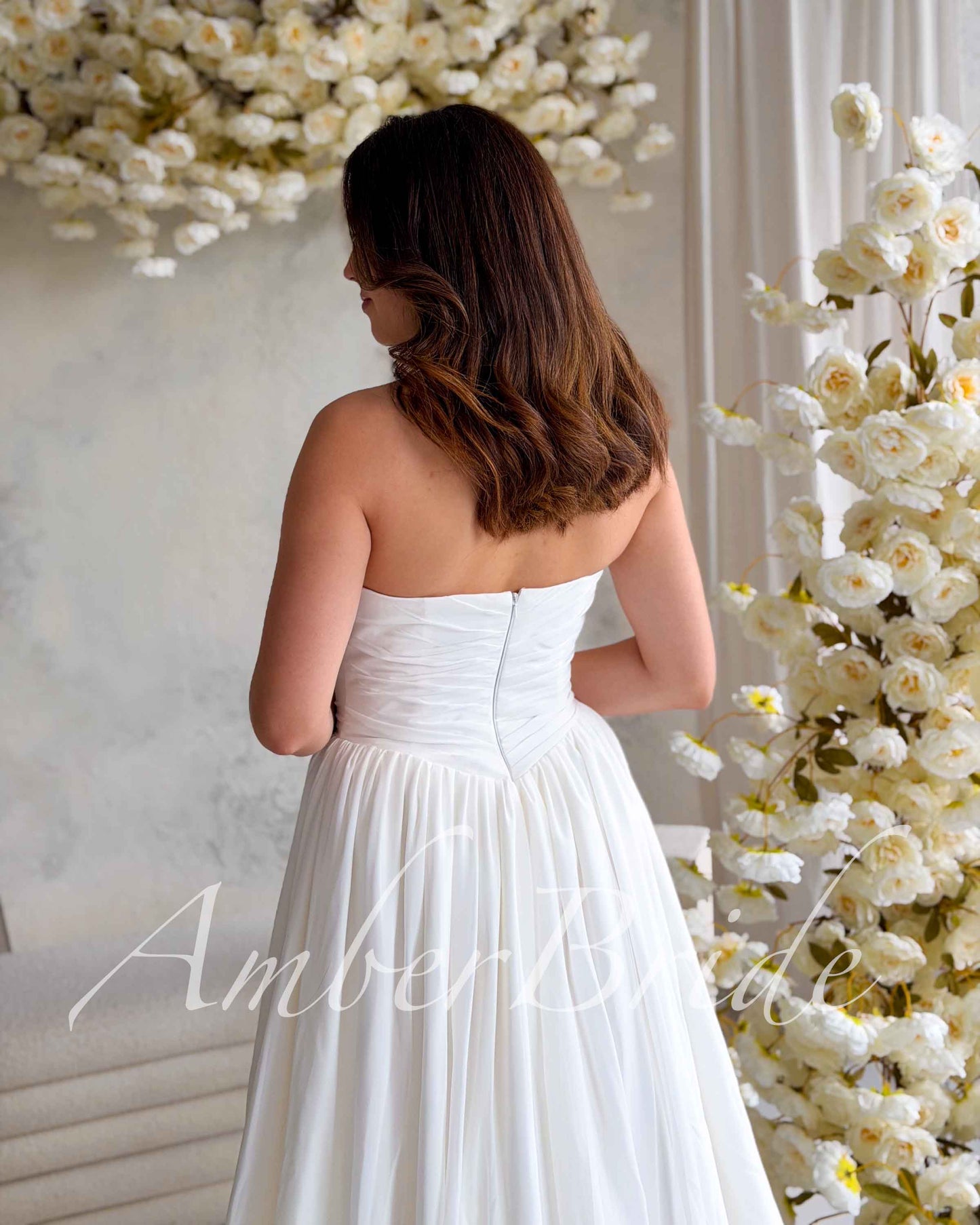 Back view of a white strapless chiffon wedding dress with a ruched bodice and a flowing A-line skirt.