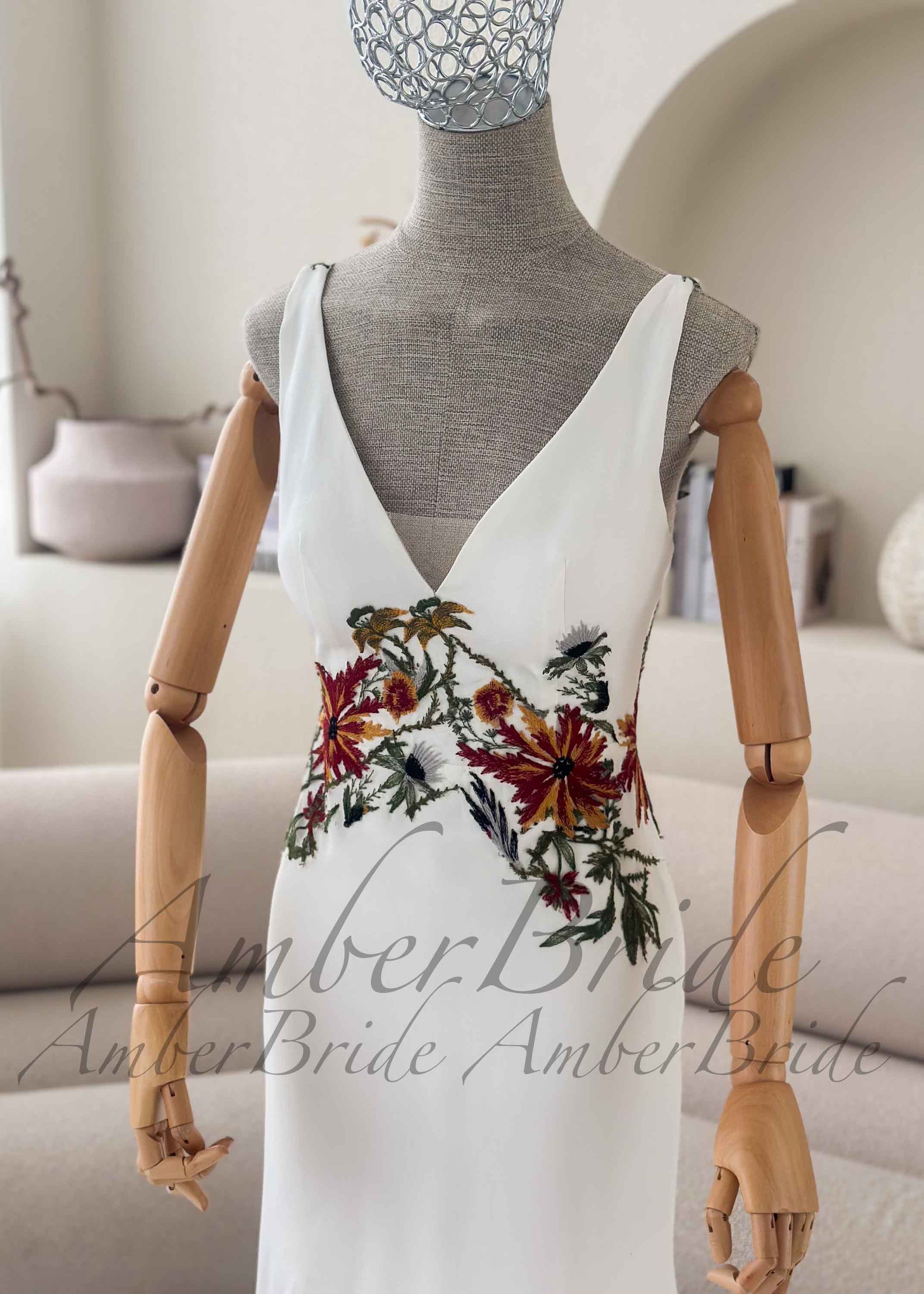 White crepe mermaid wedding dress with a deep V-neck and colorful earthy floral embroidery at the waist on a mannequin.