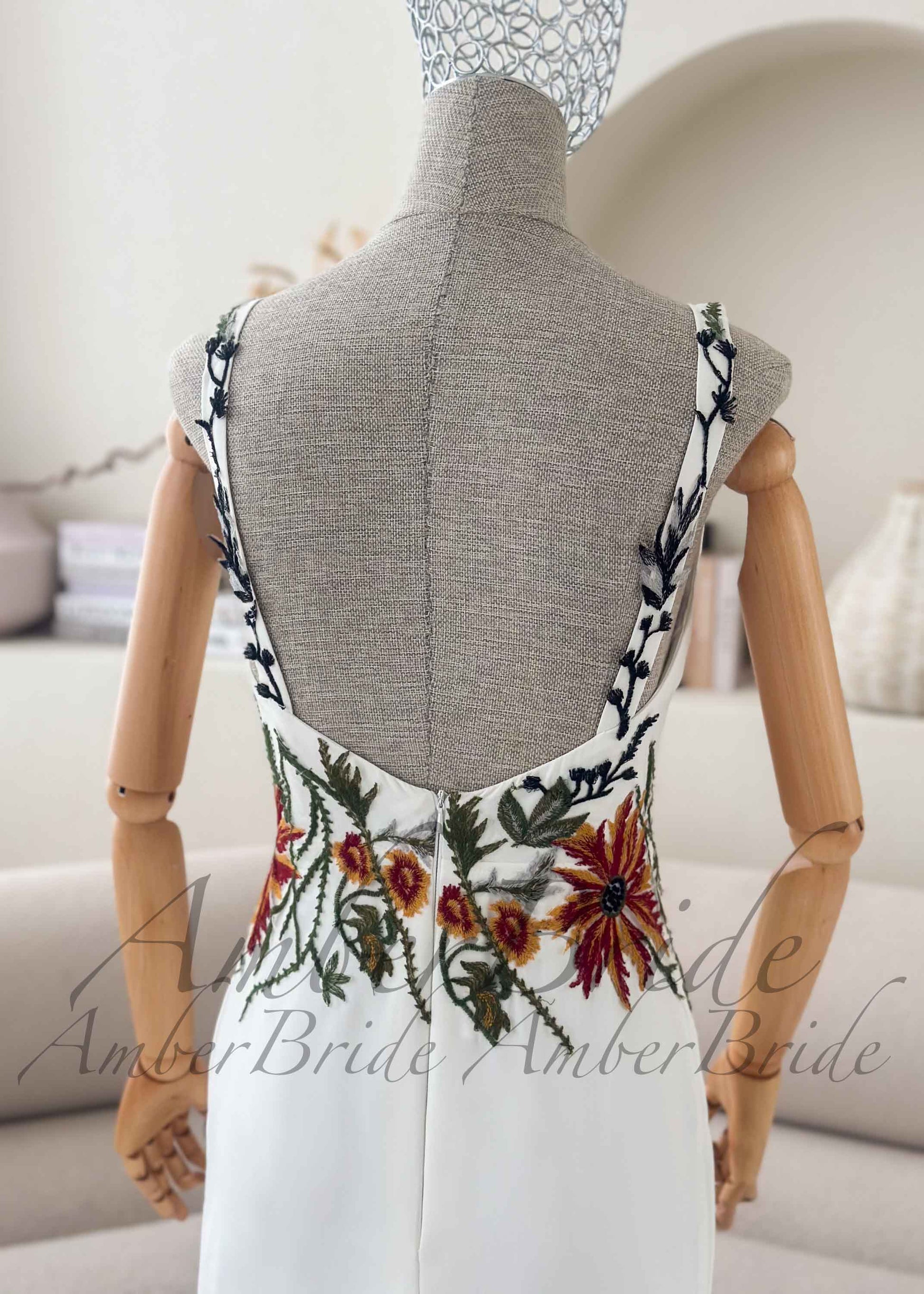 Back of white crepe wedding dress with deep scoop back and colorful earthy floral embroidery on straps and waist.