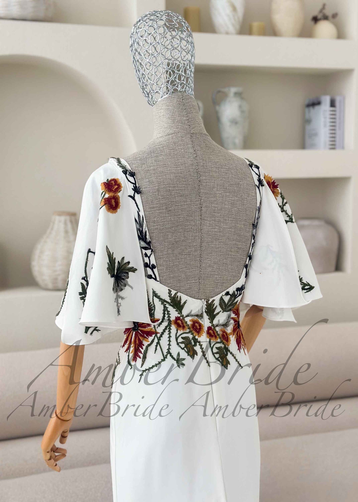 White crepe mermaid dress with a deep back, floral embroidery, and detachable flutter sleeves on a mannequin.