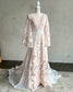 Nude boho wedding dress with white floral embroidery, V-neckline, long cape sleeves, and a defined waistline.