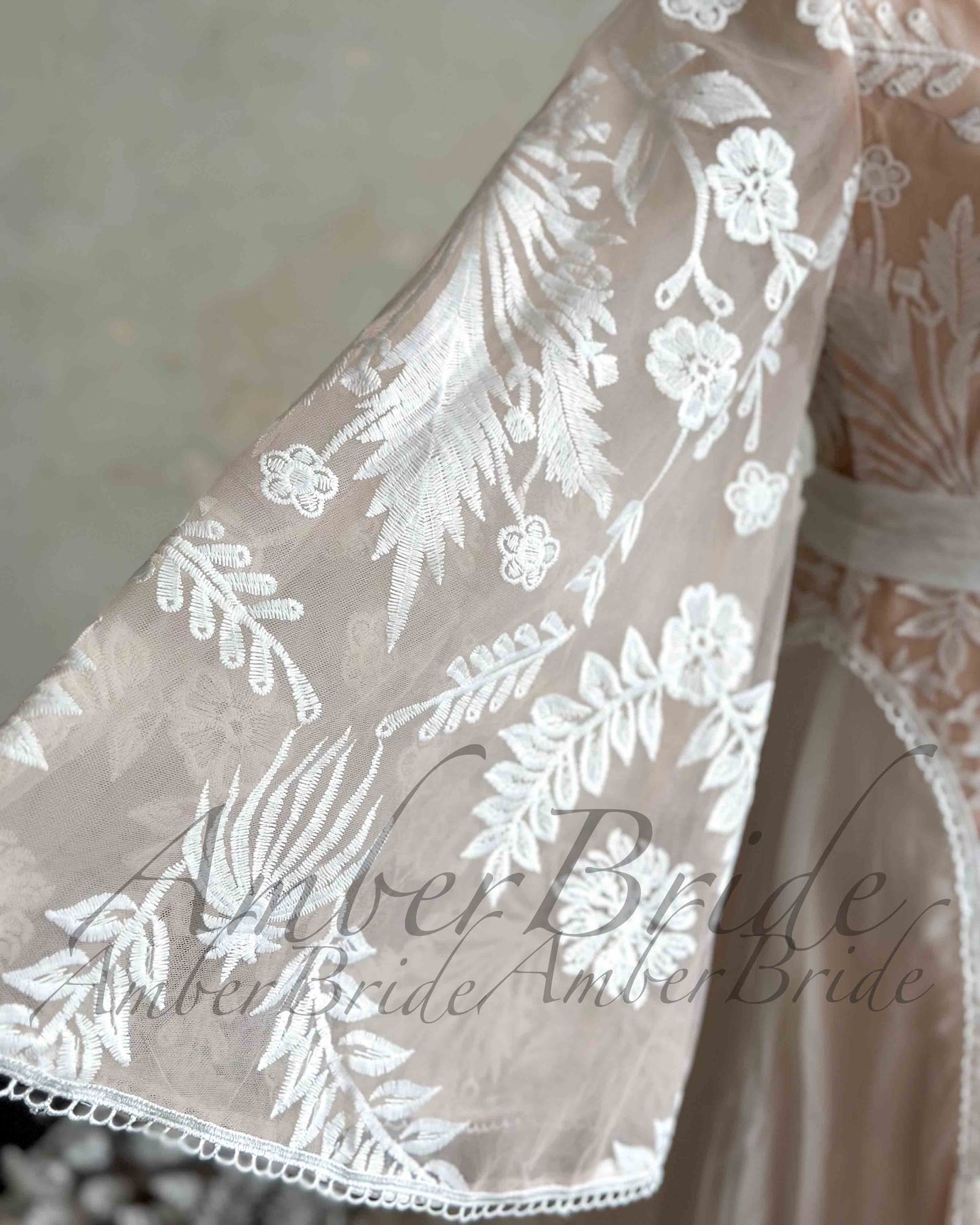 Close-up of a nude bridal dress with white floral embroidery on a sheer, flowing cape sleeve.