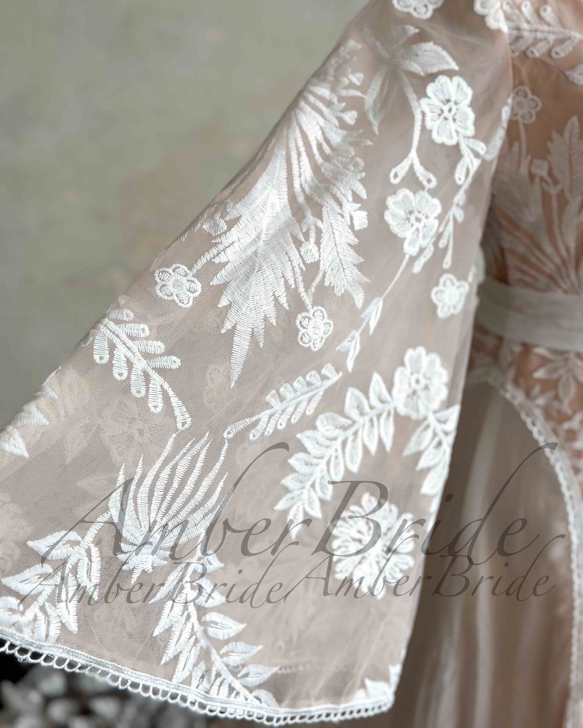 Close-up of a nude bridal dress with white floral embroidery on a sheer, flowing cape sleeve.