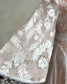 Close-up of a nude bridal dress with white floral embroidery on a sheer, flowing cape sleeve.