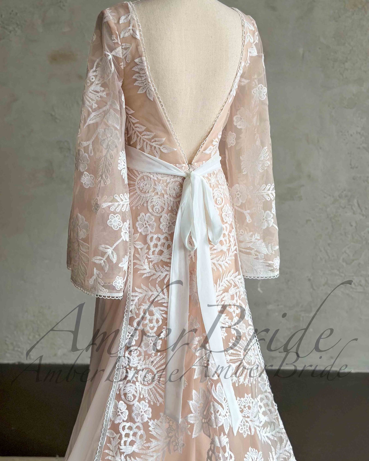 Back view of boho wedding dress with white floral embroidery, cape sleeves, open back, and a white waist tie ribbon.