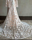 Boho wedding dress with a peach-toned slip, white floral embroidery, cape sleeves, and a long, flowing lace train.