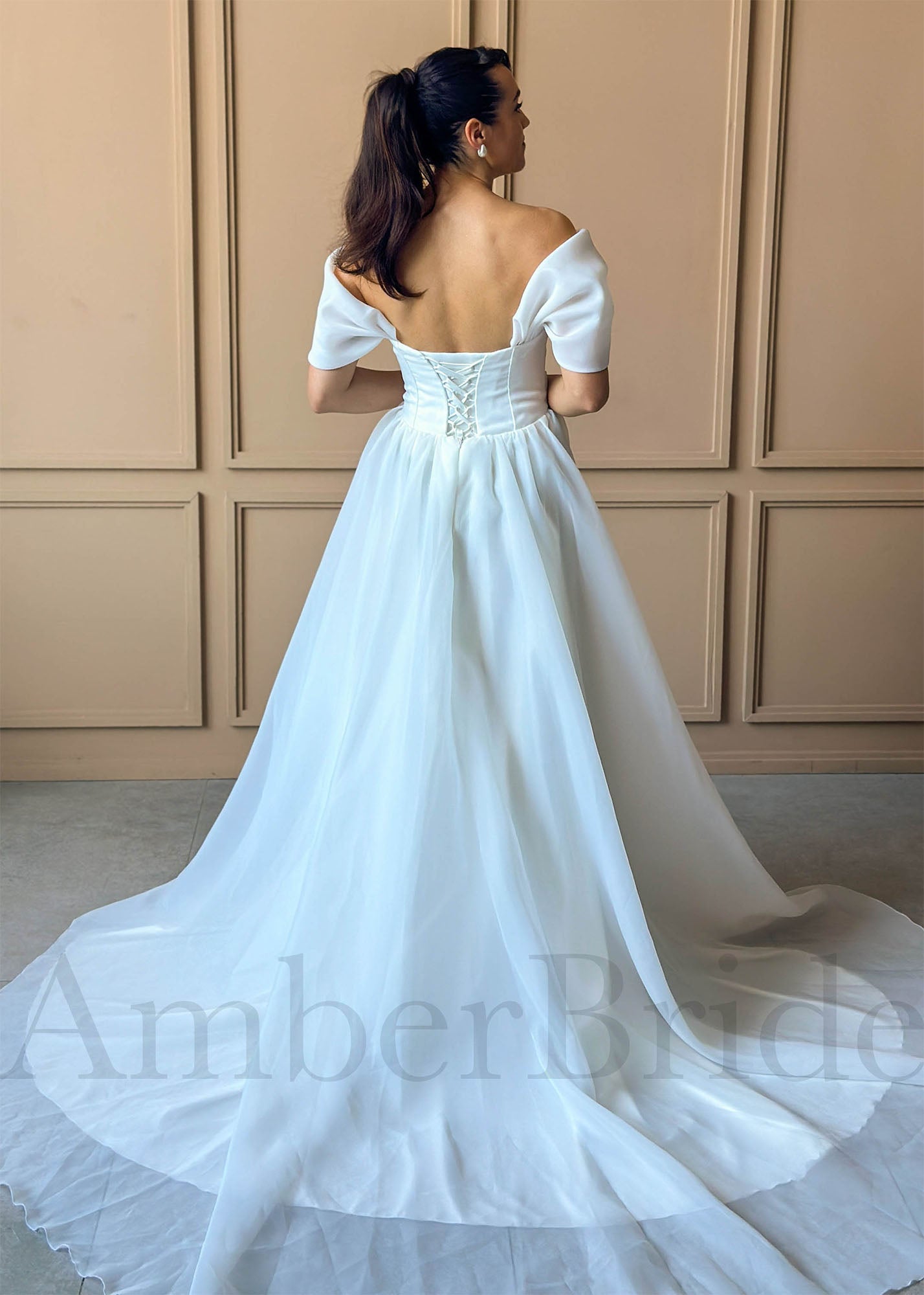 White A-line organza wedding dress with off-shoulder sleeves, corset back, and a full, flowing skirt.