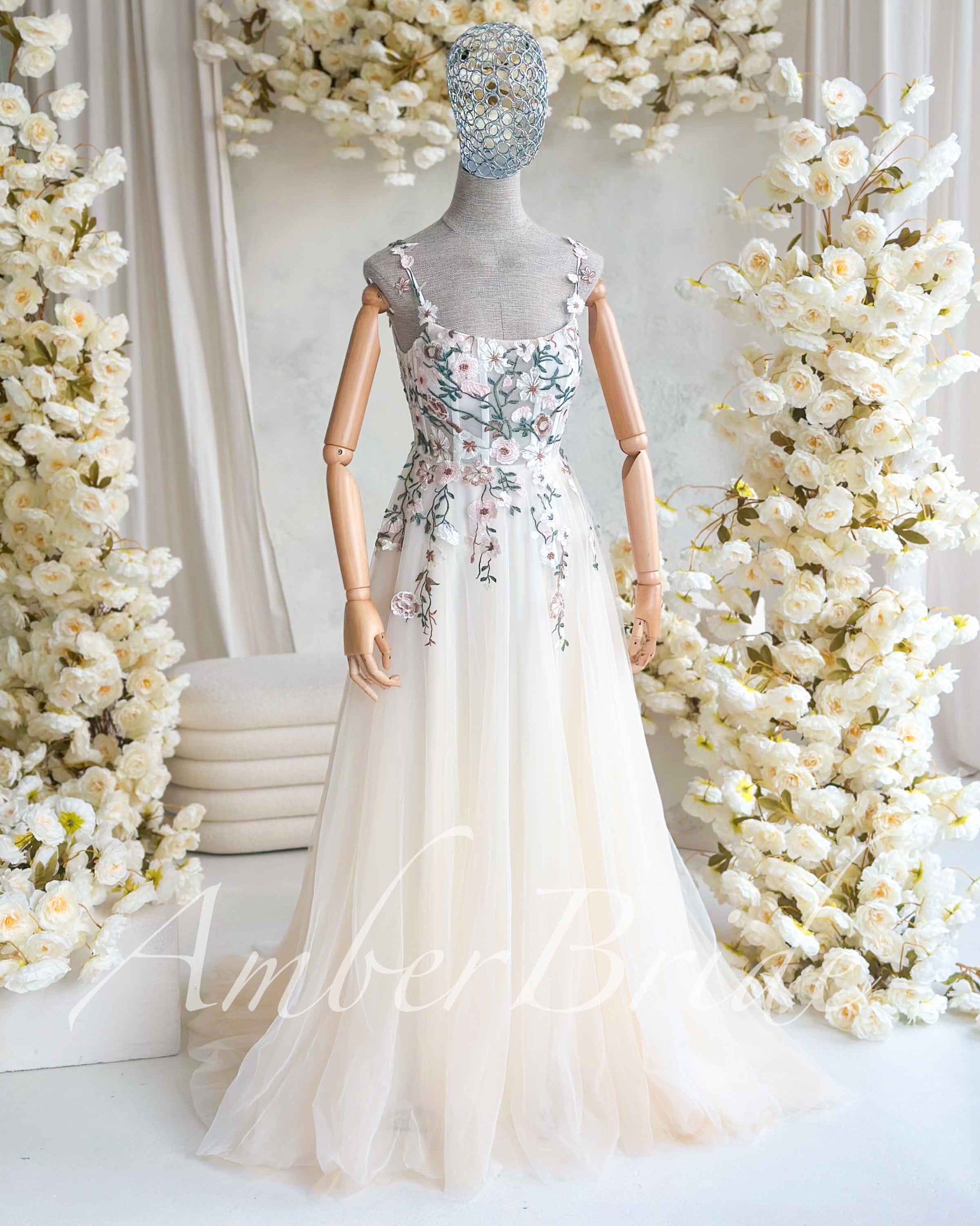 Nude A-line wedding dress with a square neckline, floral pastel embroidery, and a flowing tulle skirt on a mannequin.