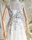 Nude wedding dress on a mannequin with square neckline, spaghetti straps, and pastel floral embroidery on tulle.