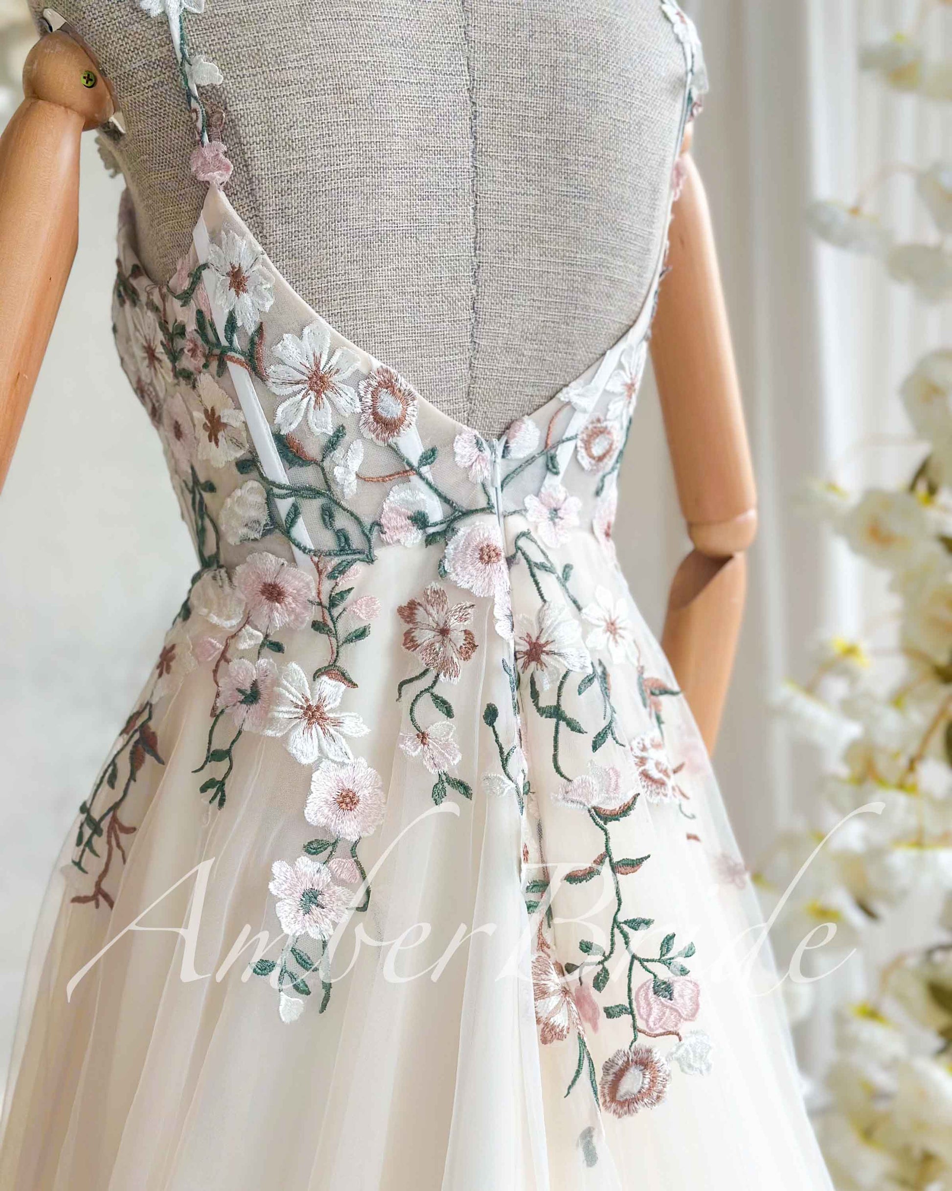 Nude wedding dress with thin straps, open back, and floral embroidery in pastel pink and green on tulle.