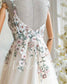 Nude wedding dress with thin straps, open back, and floral embroidery in pastel pink and green on tulle.
