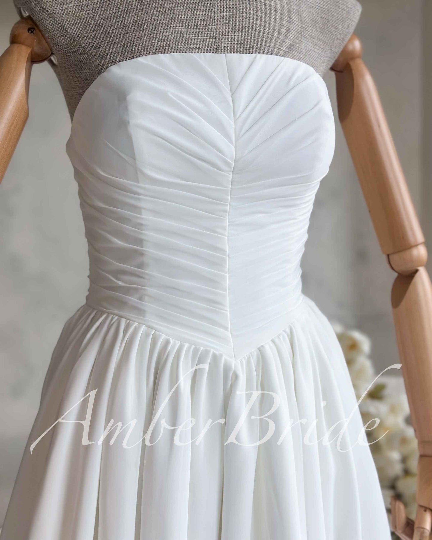 White strapless chiffon wedding dress on a mannequin, featuring a sweetheart neckline and a fitted, ruched bodice.