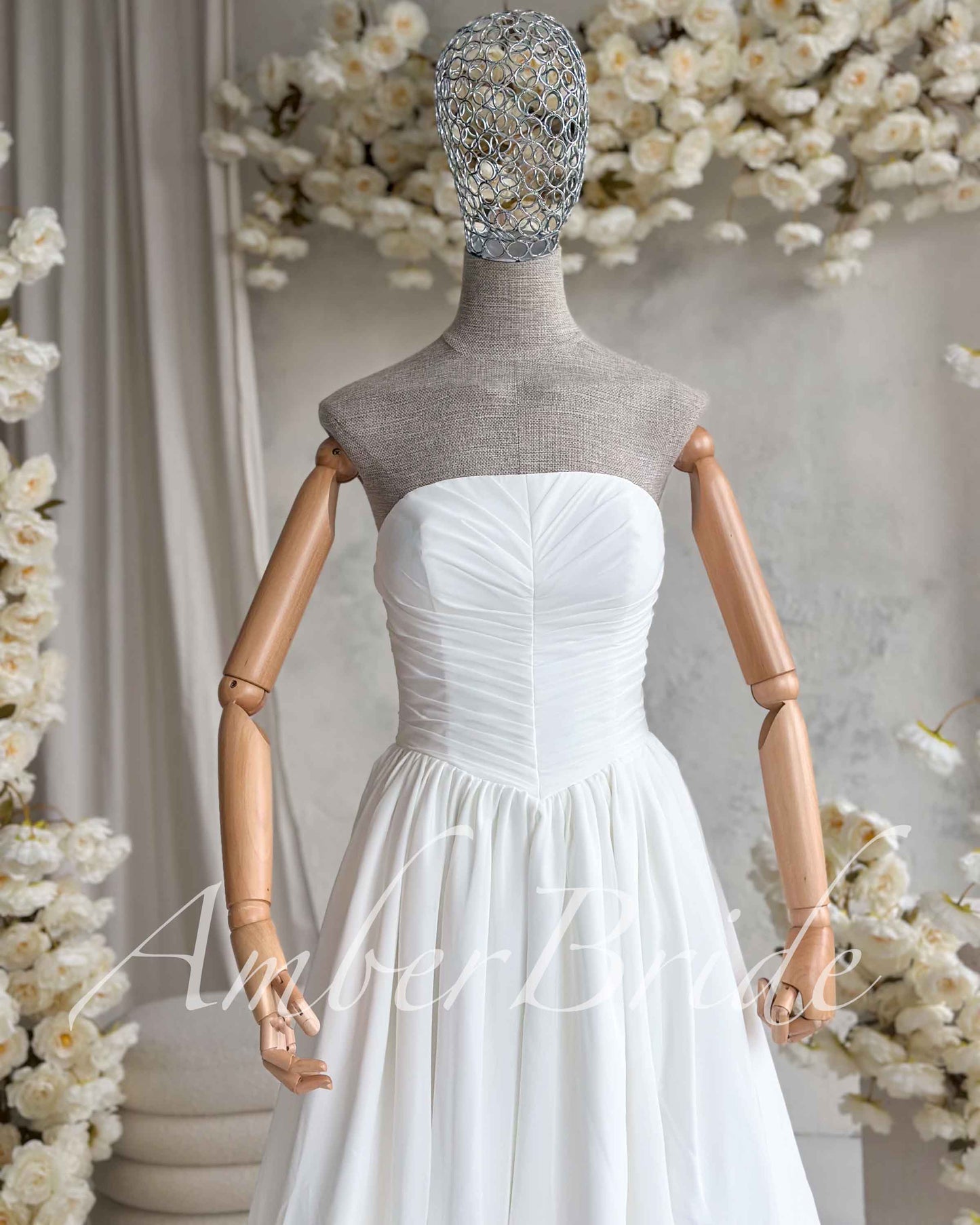 White strapless wedding dress on a mannequin featuring a ruched bodice and a flowing, lightweight chiffon skirt.