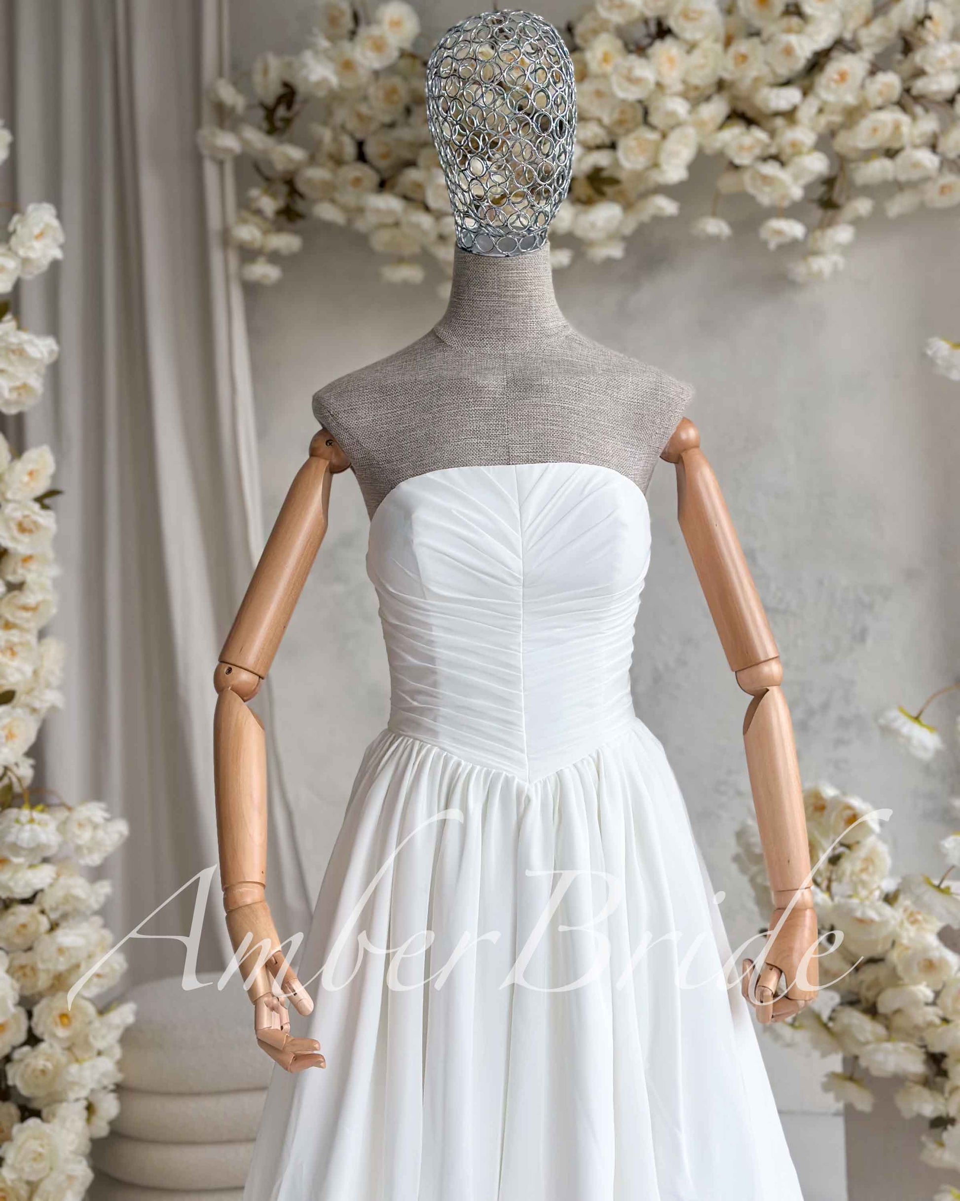 White strapless wedding dress on a mannequin featuring a ruched bodice and a flowing, lightweight chiffon skirt.