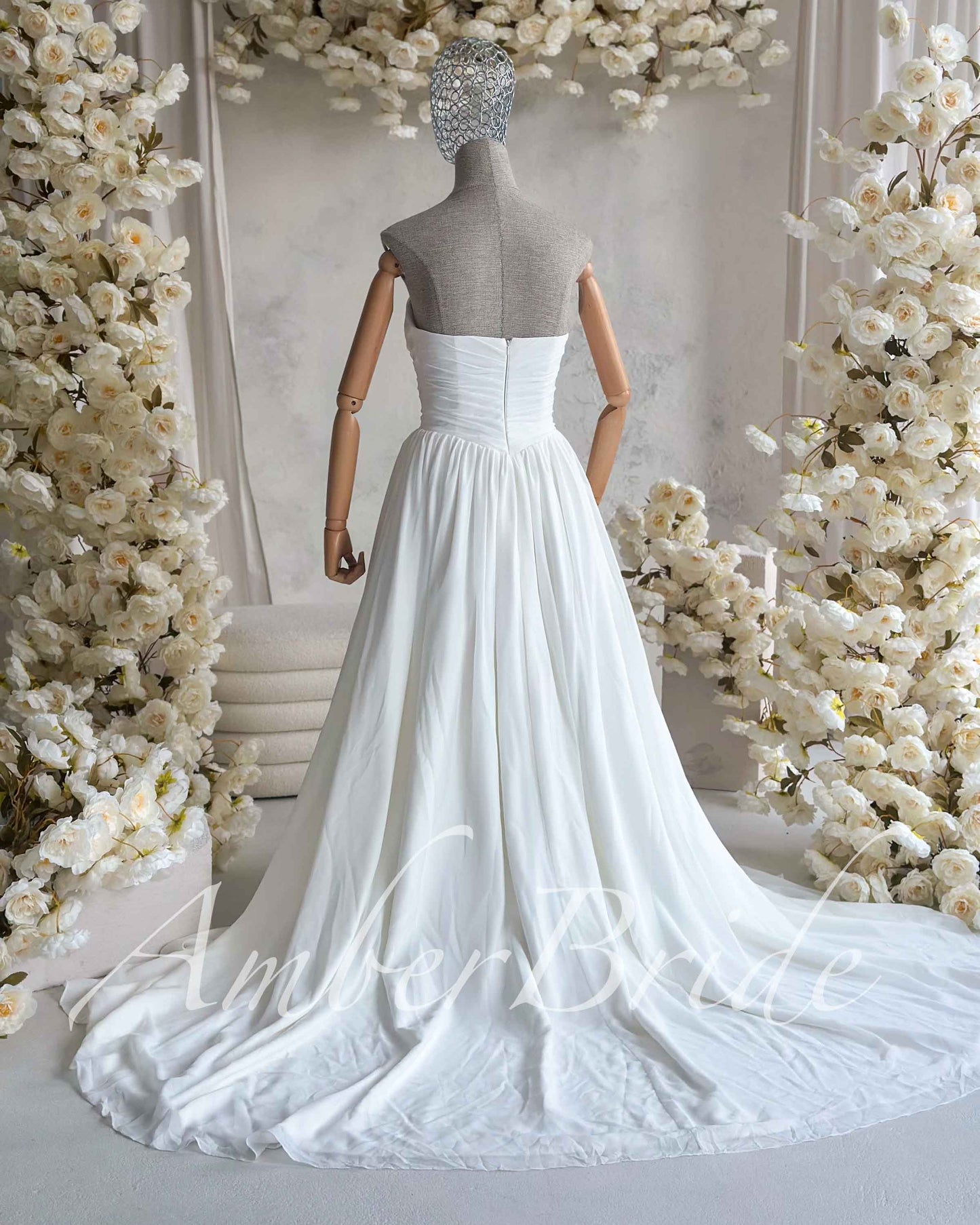 Back view of a white strapless chiffon wedding dress on a mannequin, featuring a ruched bodice and flowing skirt.