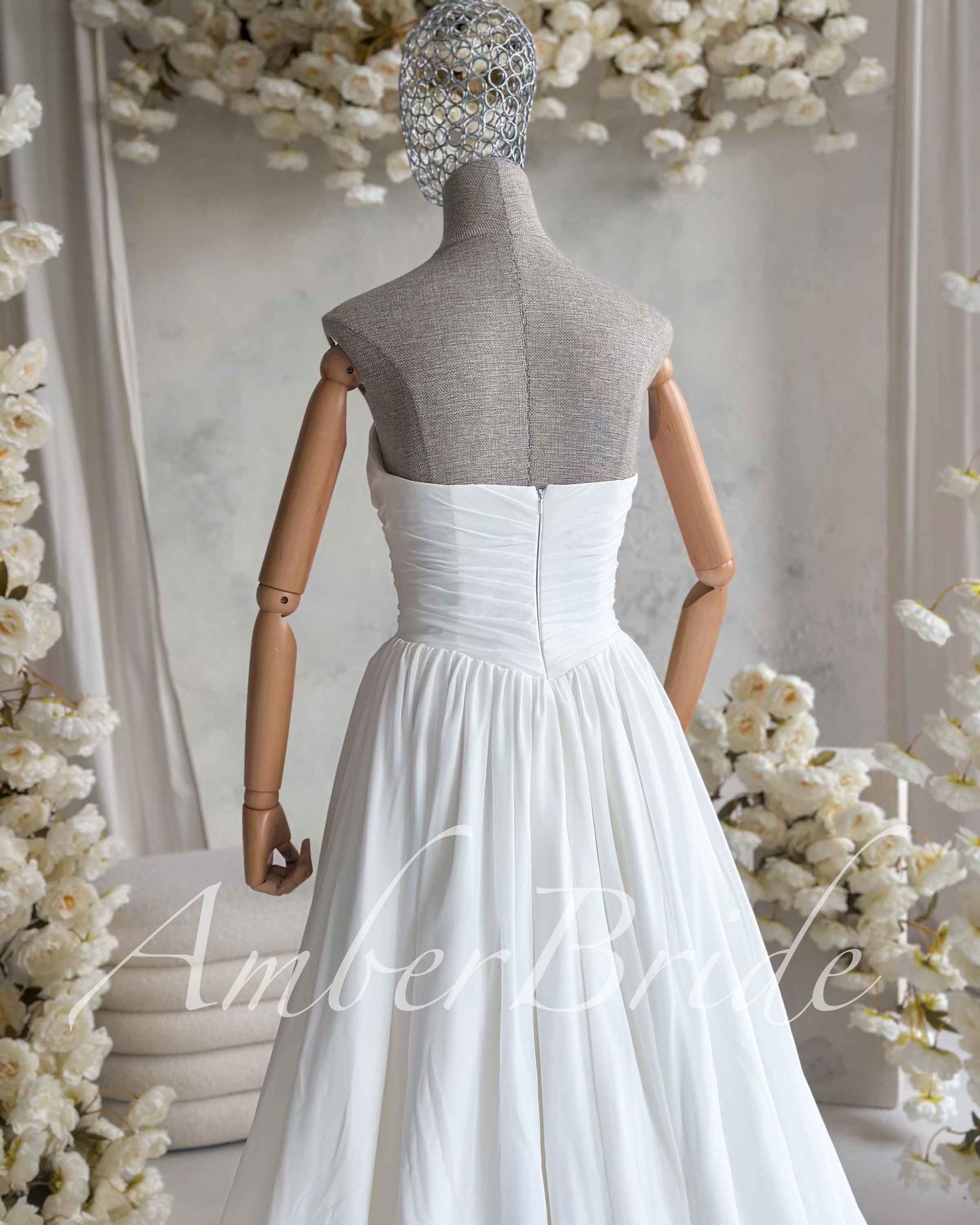 Back view of a white, strapless chiffon wedding dress on a mannequin with a ruched bodice and a zip closure.