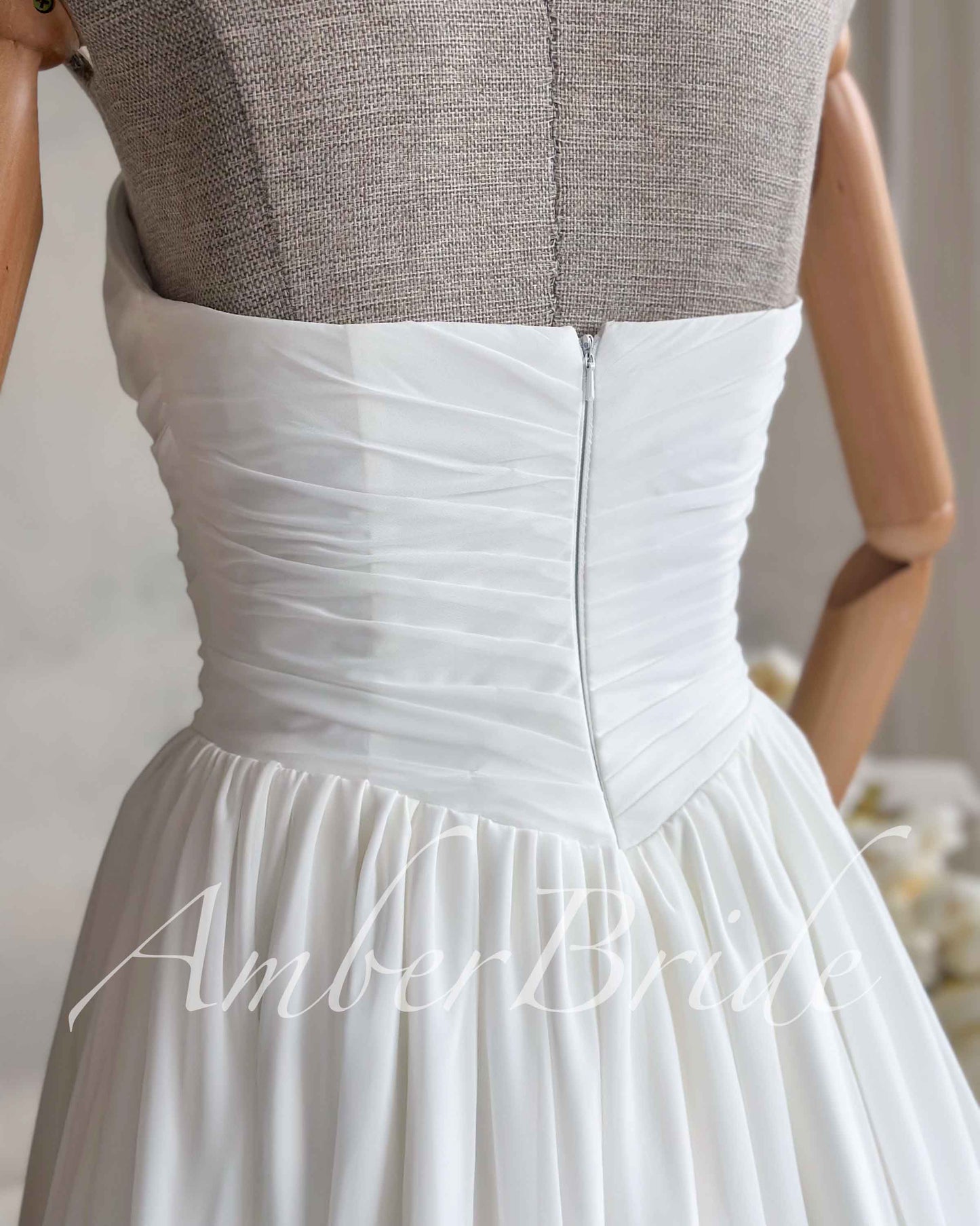 White strapless wedding dress on a mannequin featuring a ruched chiffon bodice and a center back zipper closure.