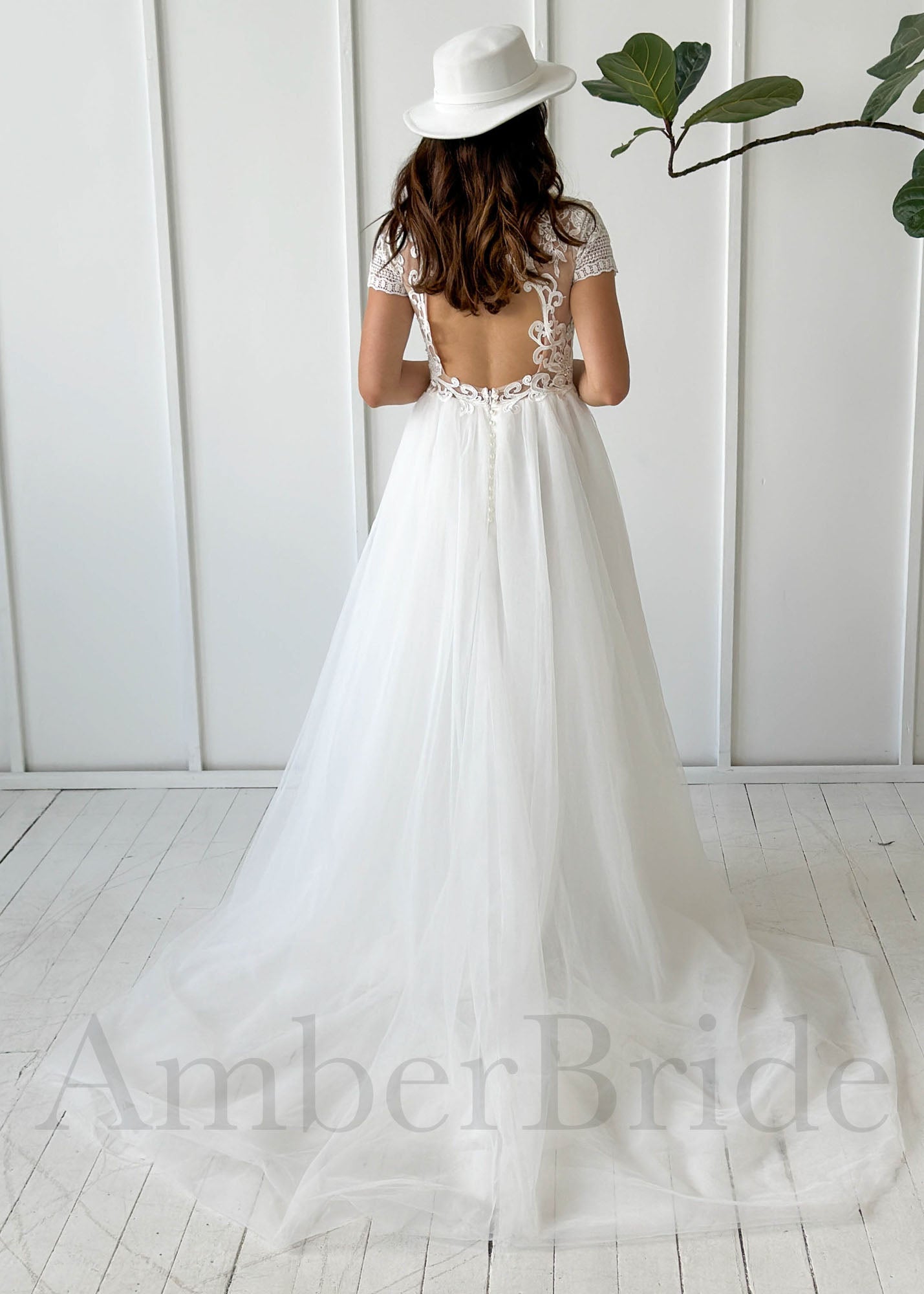 Back view of a white A-line wedding dress with a lace bodice, open back, short sleeves, and flowy tulle skirt.