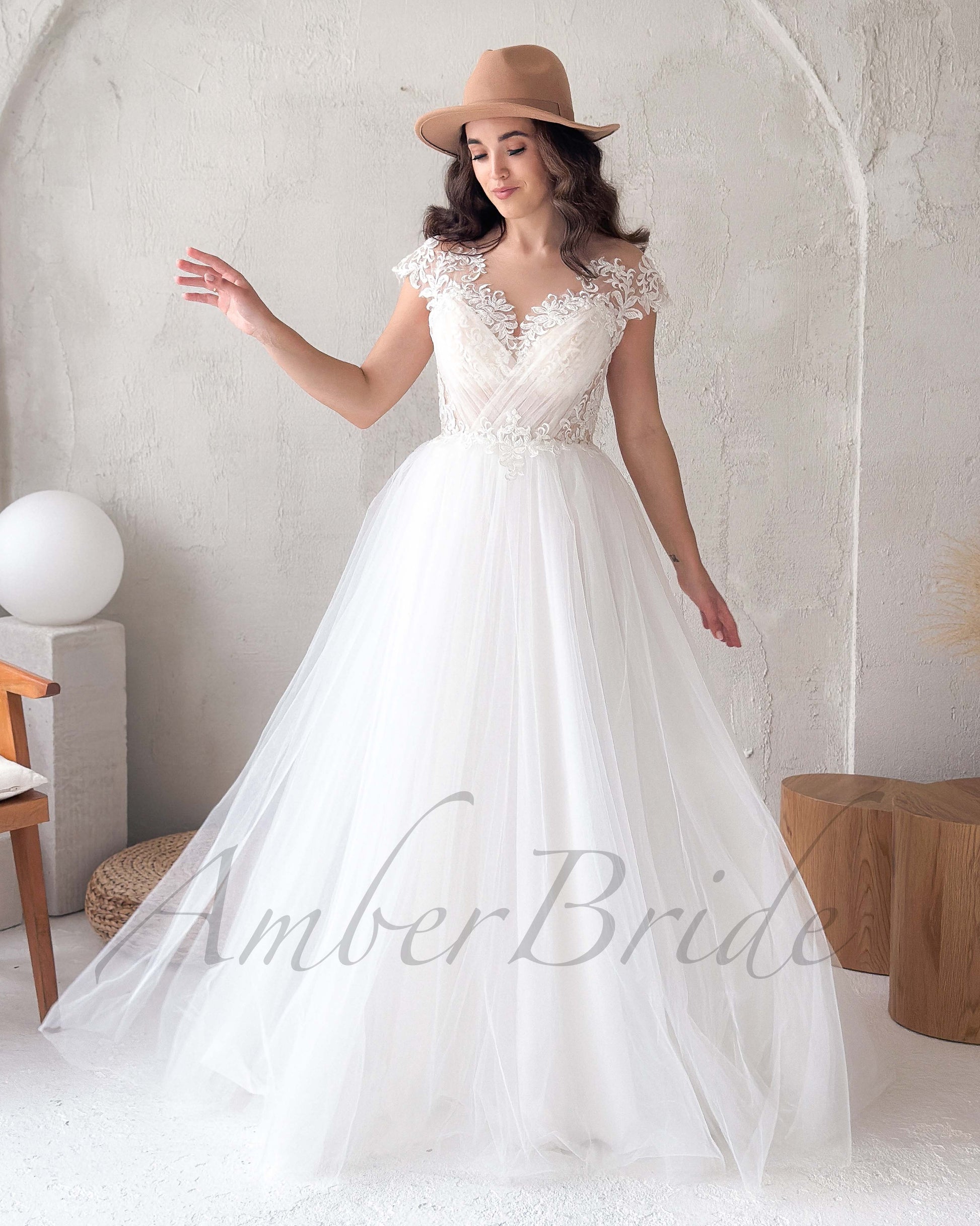 Woman wearing a boho white A-line wedding dress with a V-neck, lace bodice, cap sleeves, and a full tulle skirt.