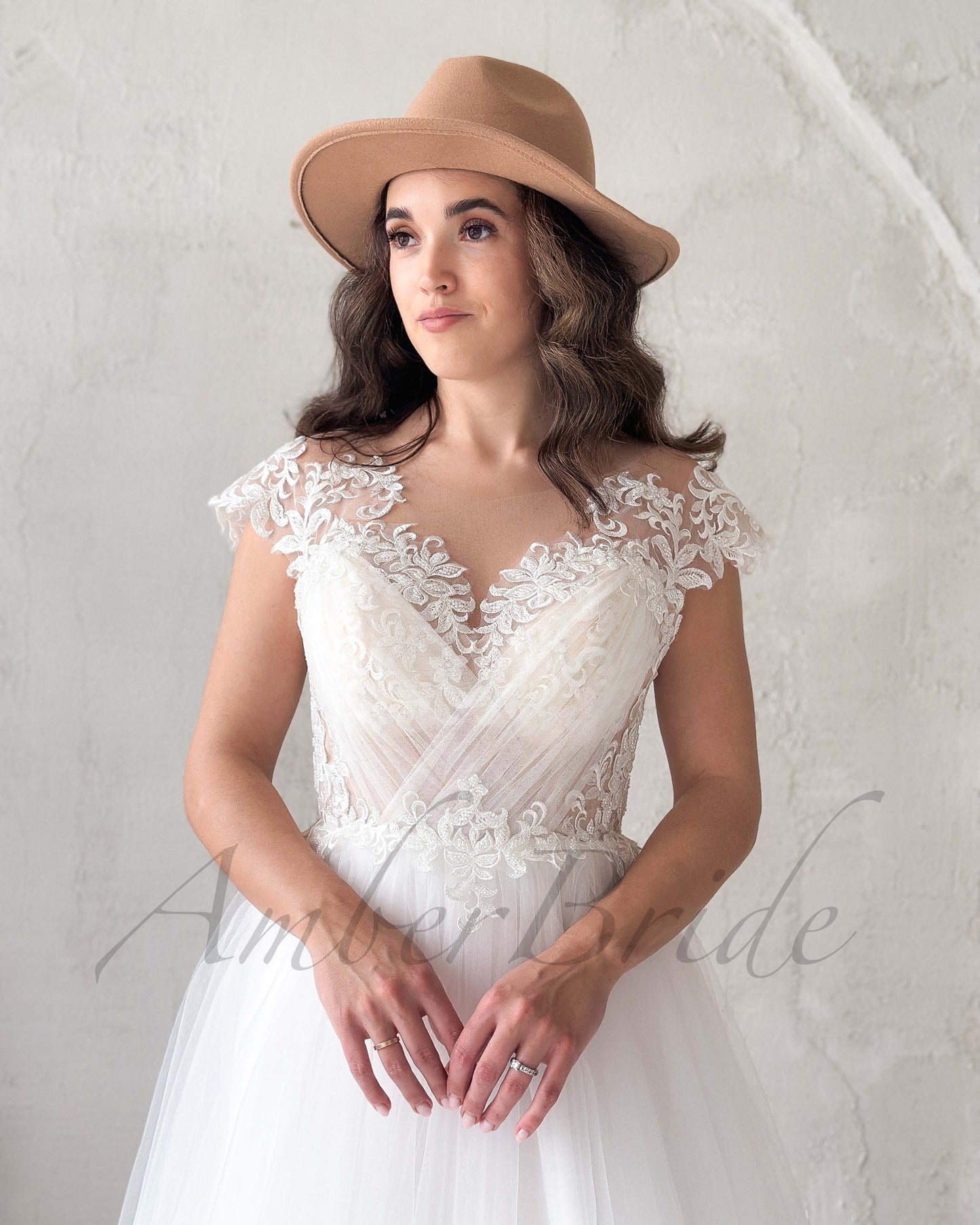 Bohemian wedding dress with V-neck, cap sleeves, illusion lace bodice, and tulle skirt, worn with a tan felt hat.