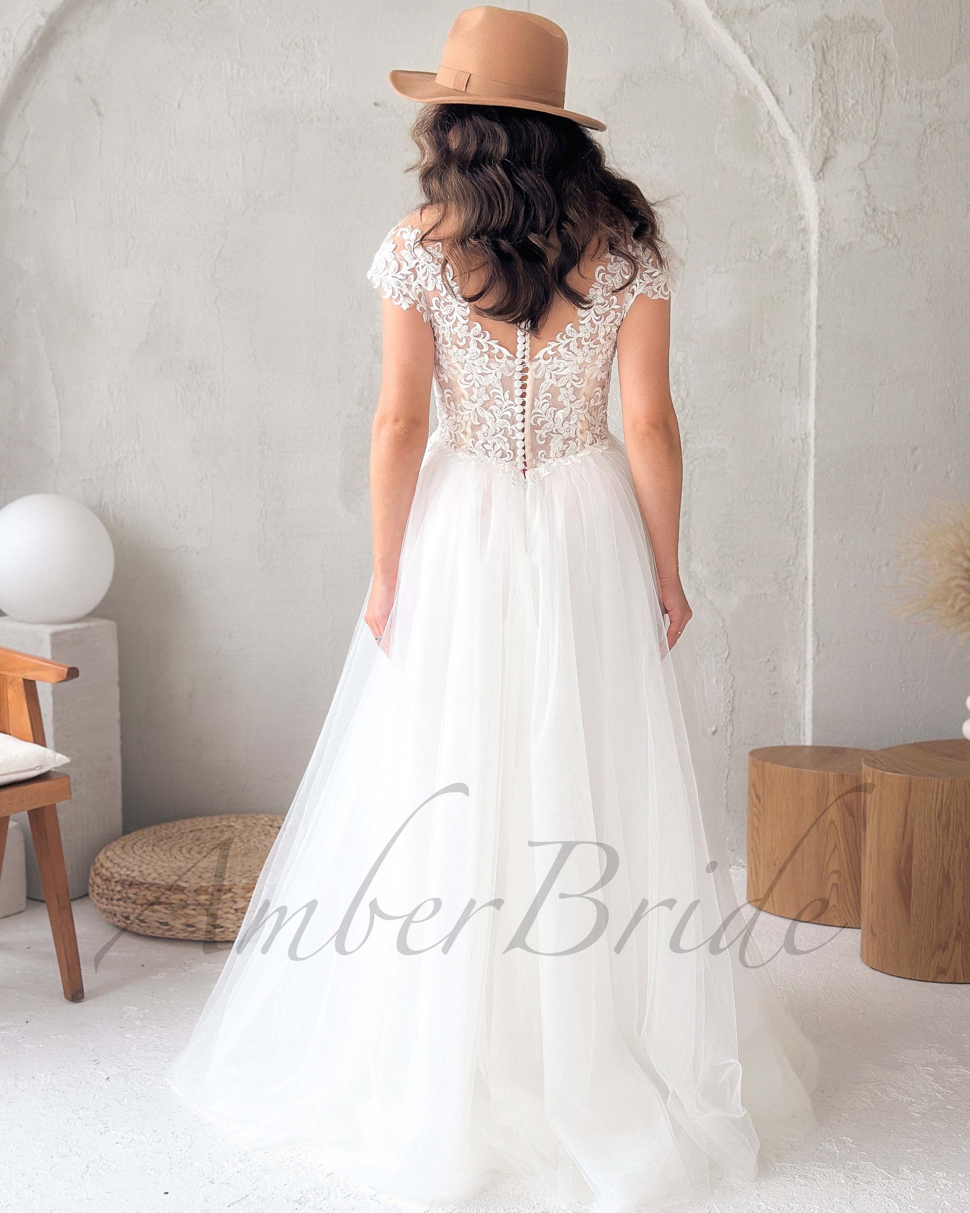 Back view of a white bridal gown with cap sleeves, illusion lace back, button detail, and a flowing tulle skirt.