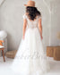 Back view of a white bridal gown with cap sleeves, illusion lace back, button detail, and a flowing tulle skirt.