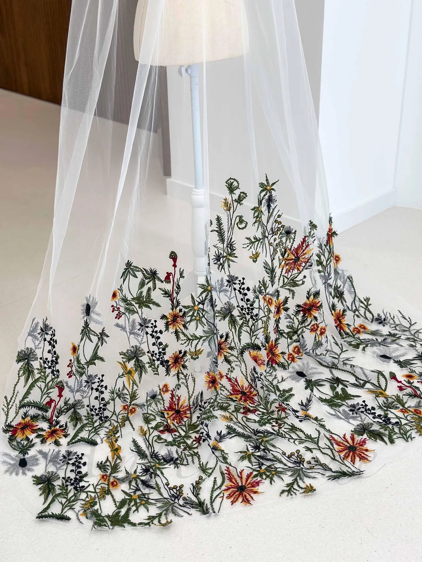 White bridal veil on a mannequin featuring colorful wildflower embroidery in red, yellow, and green on sheer tulle.