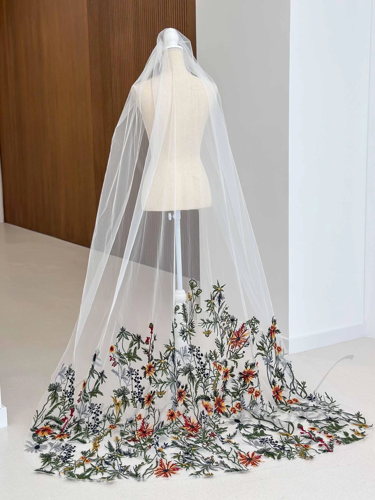 White tulle bridal veil on a mannequin featuring colorful, detailed floral embroidery along the hem.